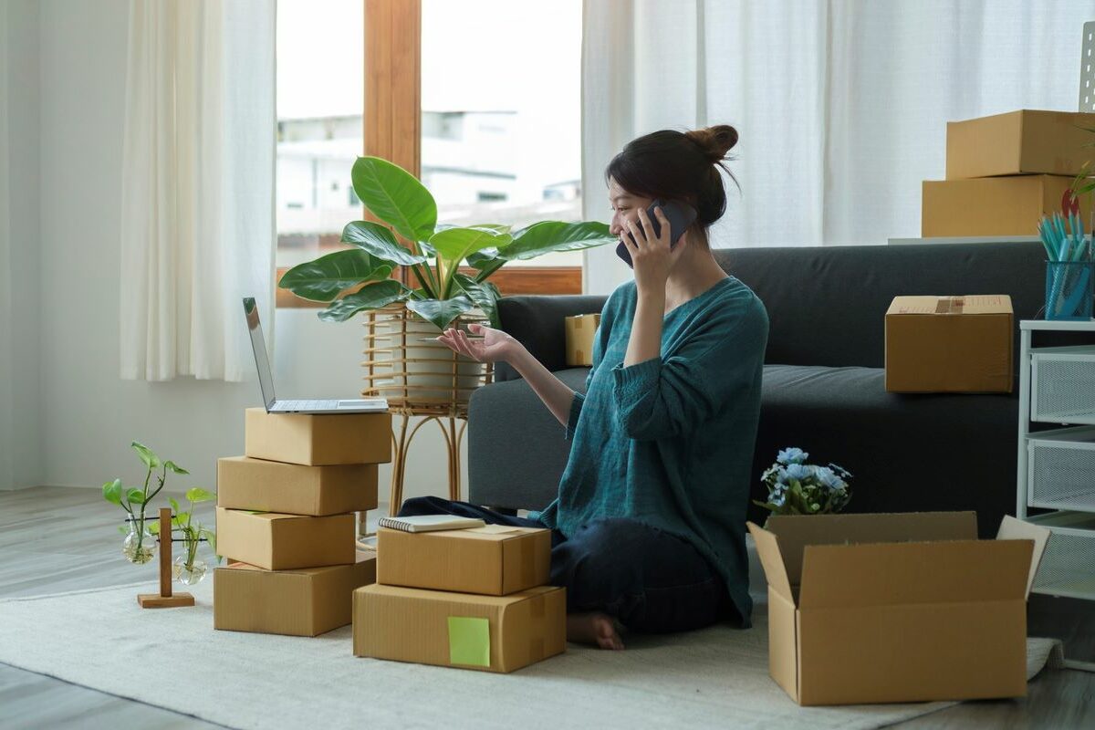 Young woman working on a laptop and handling boxes of items in her city apartment.