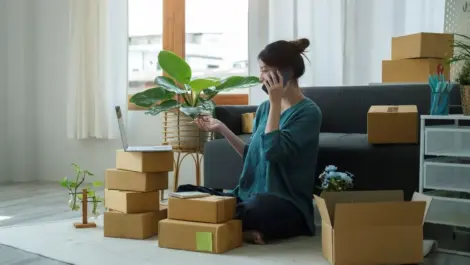 Young woman working on a laptop and handling boxes of items in her city apartment.