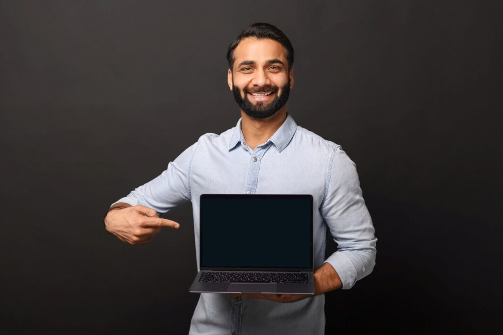 Man smiling while holding and pointing at an open laptop.