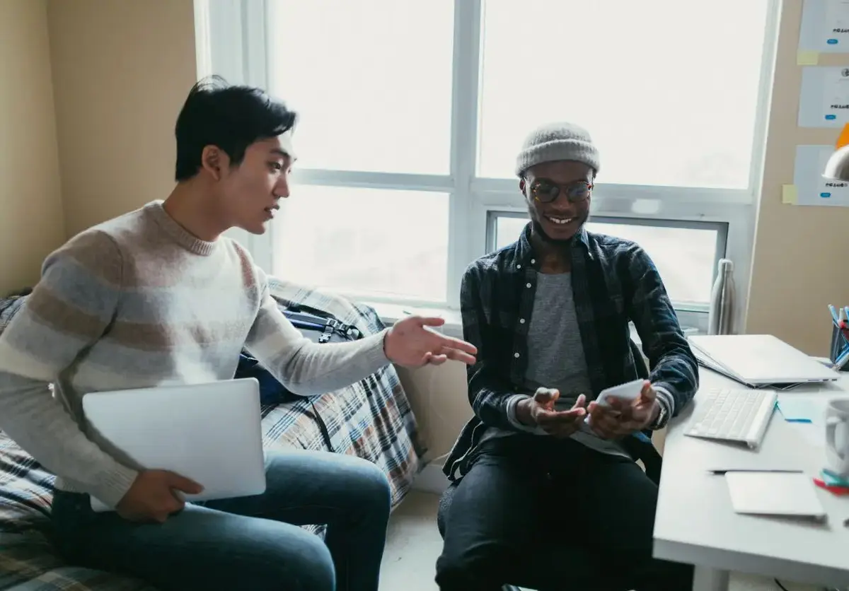 Two friends talking inside of a dorm room.