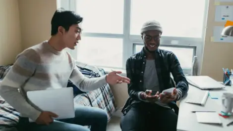 Two friends talking inside of a dorm room.