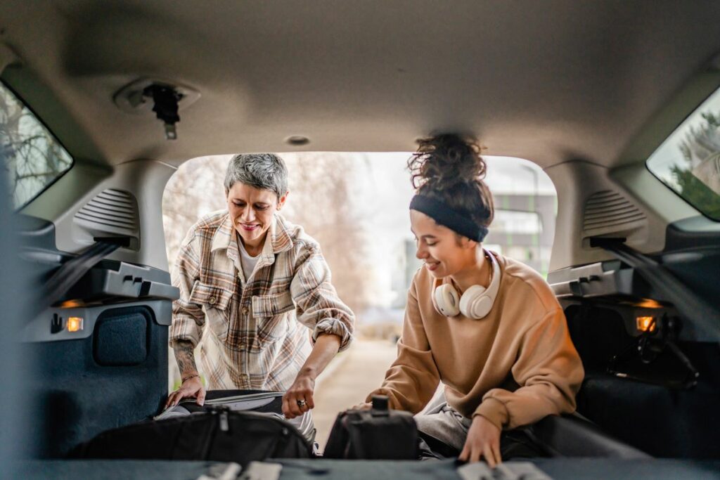 Mom helping daughter pack luggage into car for college. 