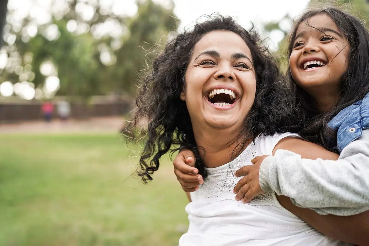 A close-up of a smiling daughter on her mother’s back at a local park.