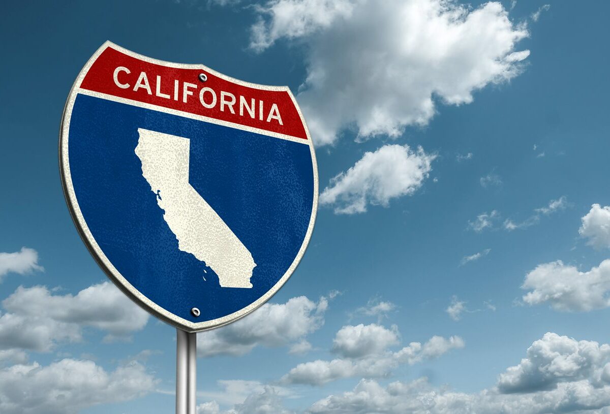 A California interstate road sign with small white clouds and a blue sky above it.