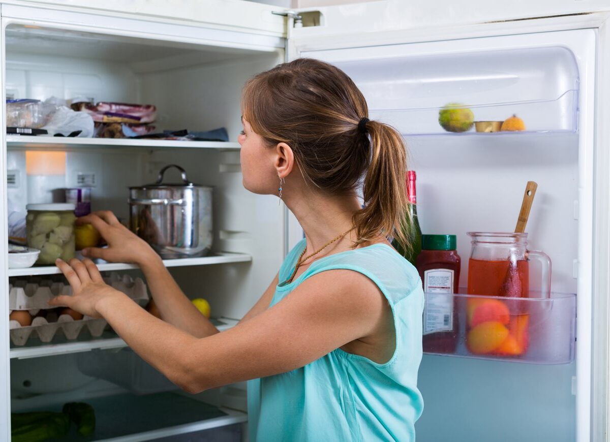 Woman placing items inside her fridge to maximize organization.