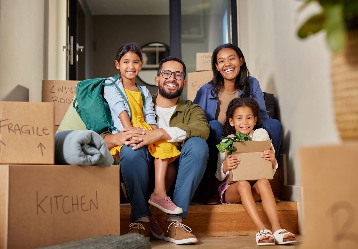 A happy family surrounded by boxes sits on their new house's front steps.