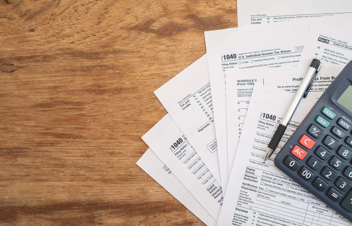 United States tax forms, a calculator, and a pen spread across a wooden table for tax season.