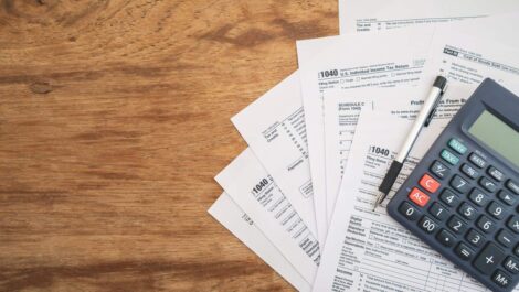 United States tax forms, a calculator, and a pen spread across a wooden table for tax season.