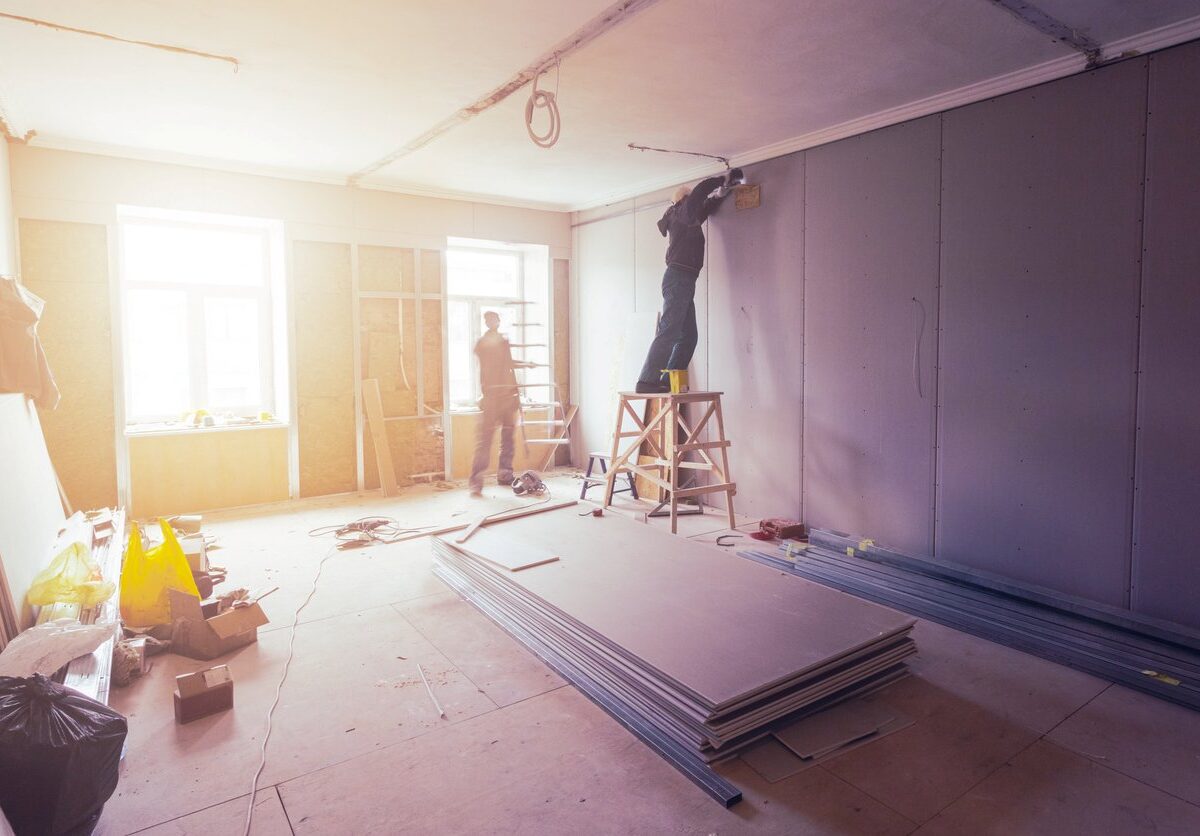 Workers install drywall in a house as the evening sun shines through the window.