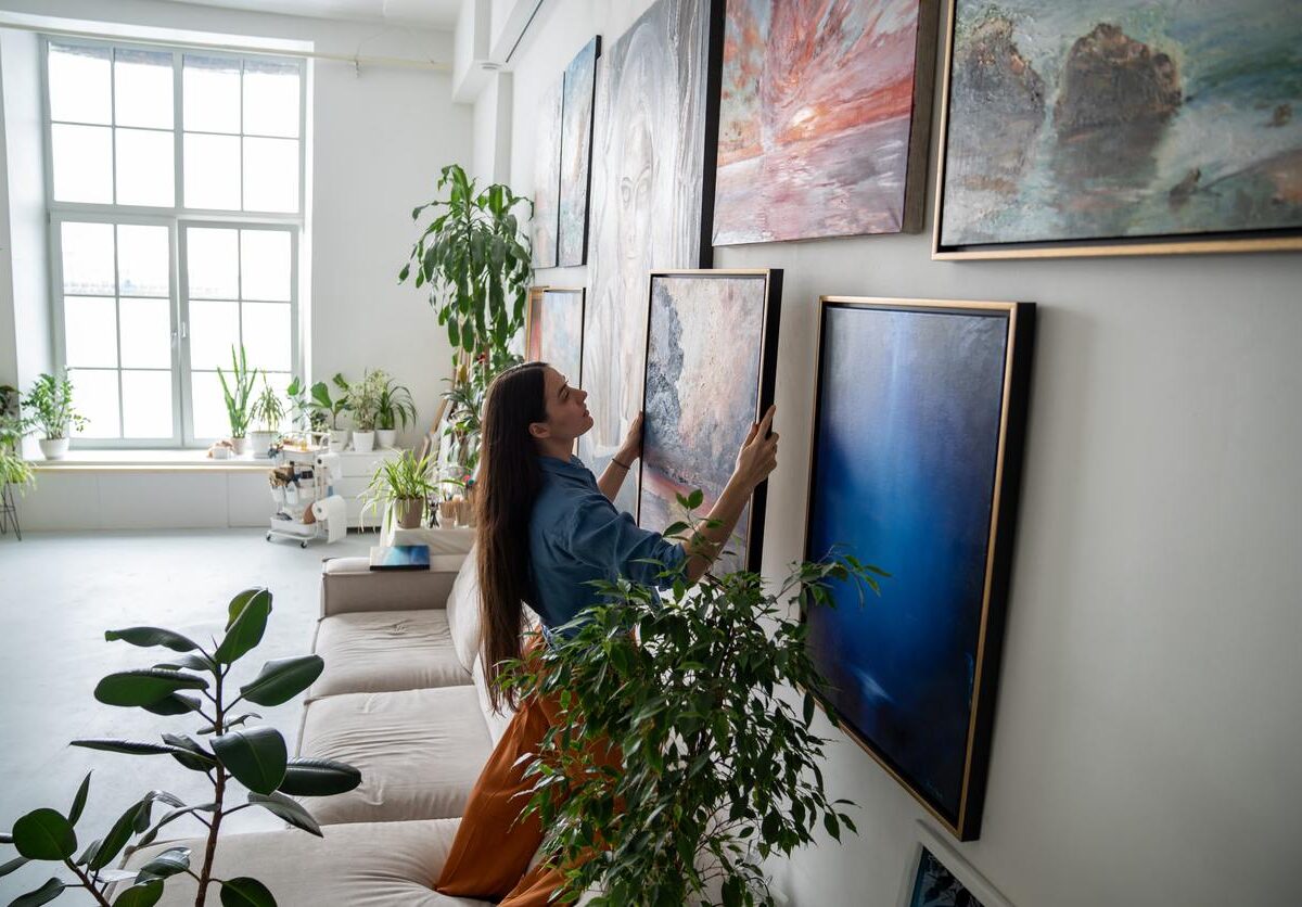 A woman hanging colorful artwork on the wall.