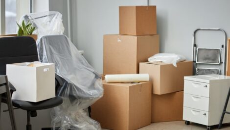 Packed boxes, cabinets, office chairs, and other office furniture are stacked against a wall for an office relocation.